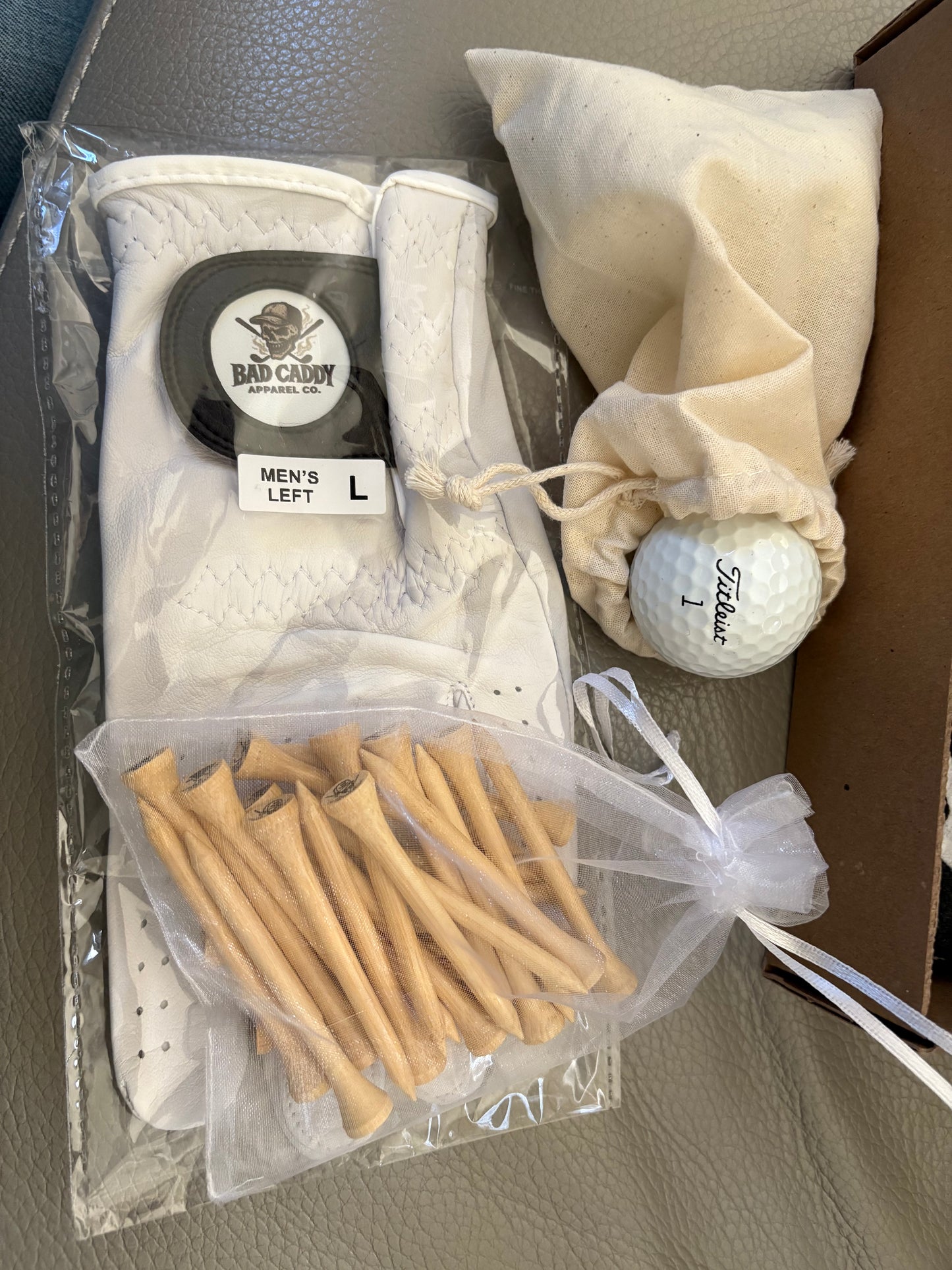 Golf accessories including a glove, golf balls, and tees in packaging on a gray surface.
