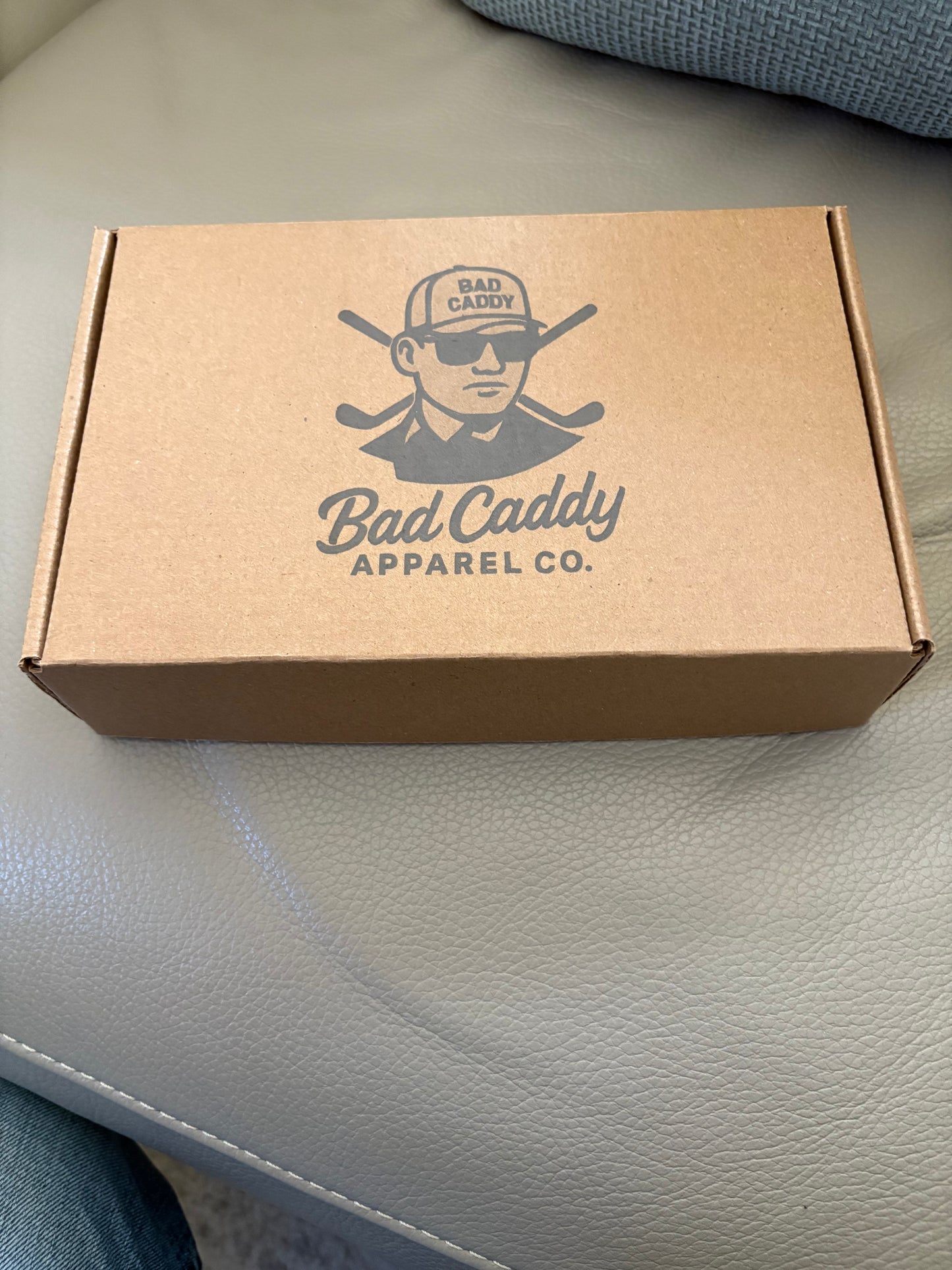 Brown cardboard box with 'Bad Caddy Apparel Co.' logo on a light gray surface.